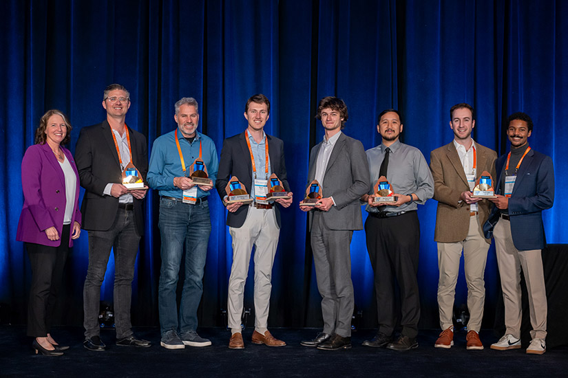 20250421-record-attendance-at-30th-annual-nrel-industry-growth-forum-as-innovation-soars-winners Several people stand on a stage posing for the camera, many of them holding awards.