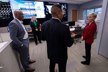 Four people stand in room with large display monitors