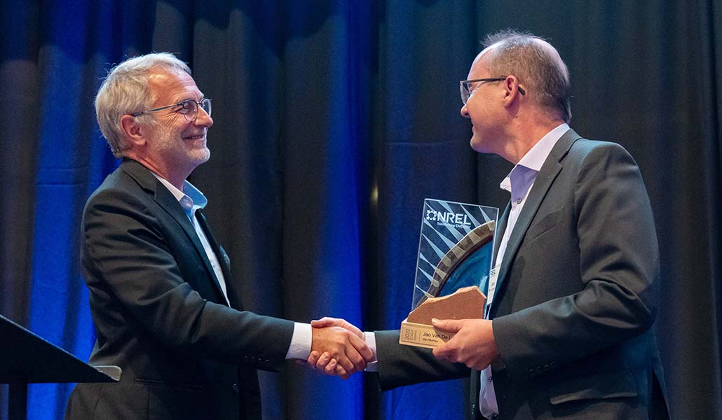 Two people shake hands, one of whom holds a plaque.