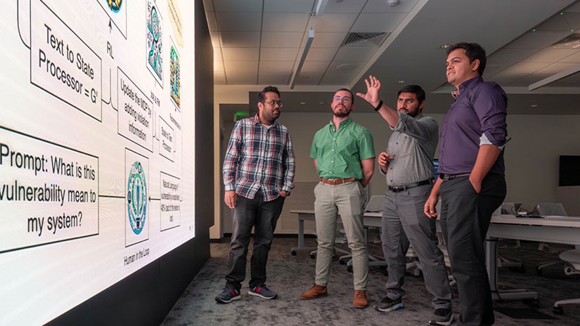 cyber-workforce Four people stand and look at flow chart on large display screen