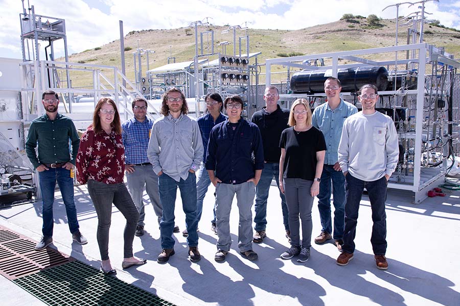 Group of people stand outside in front of transmission lines infrastructure.