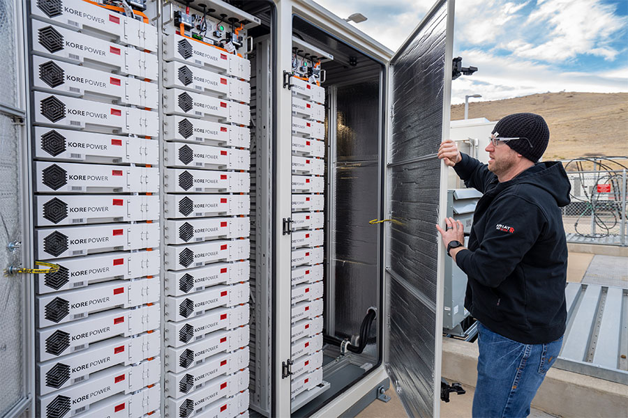 Person stands outside at research facility and opens door to KORE Power energy storage unit filled with lithium iron phosphate batteries.