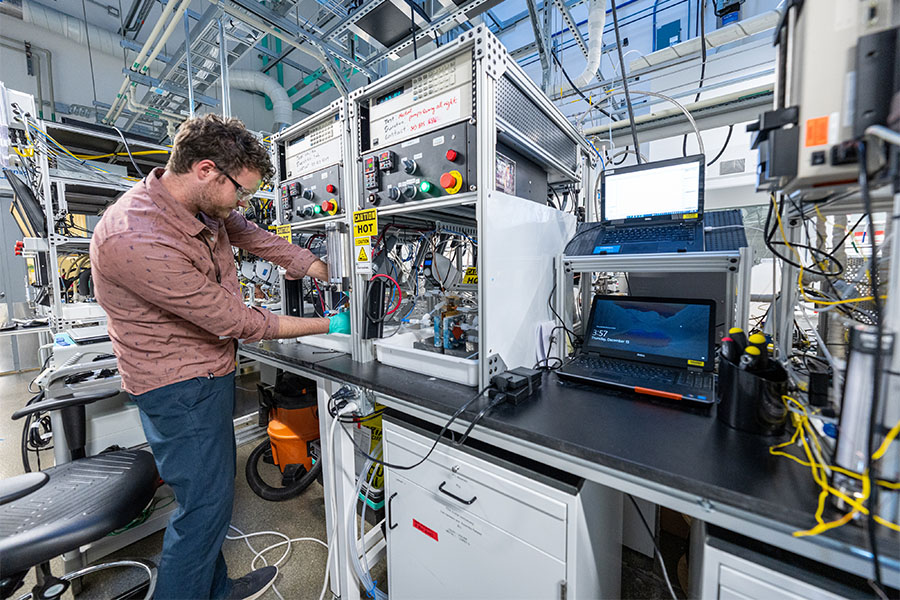 Chemistry researcher stands inside lab working over table testing low-temperature electrolysis.