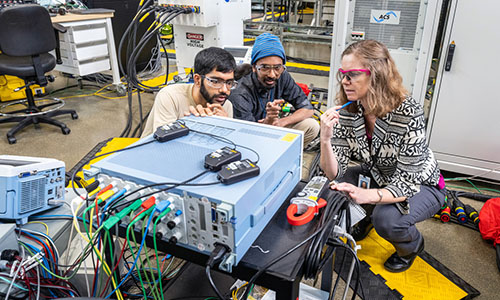 Three people look at computer system inside laboratory.