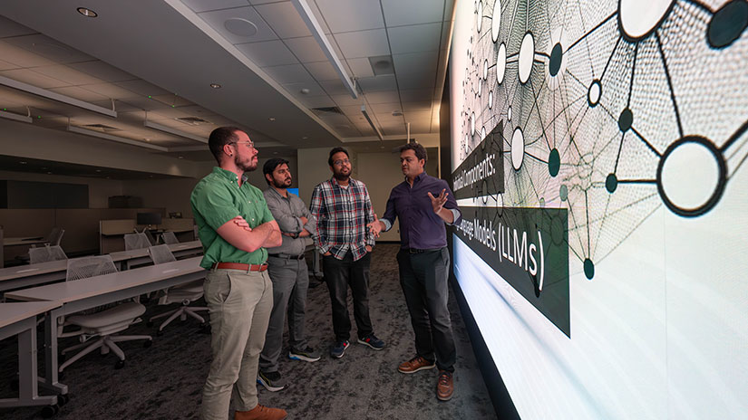 People standing in front of large display screen having a discussion