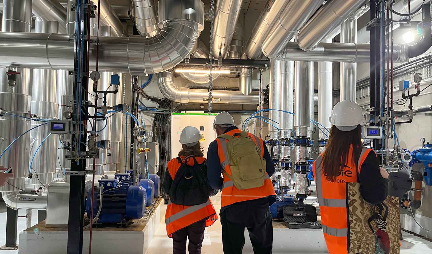 workers in orange vests surrounded by heat pumps