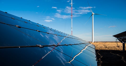 Solar panel with a wind turbine in the background.