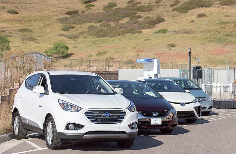 Photo of four vehicles lined up side by side next to a hydrogen fueling station.