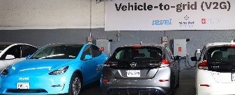 Four cars parked next to charging units with a sign reading "Vehicle-to-grid (V2G)."