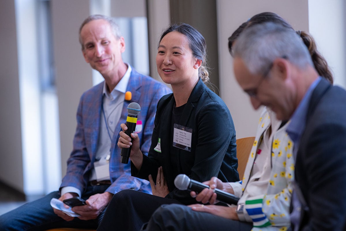 A woman speaks with a microphone as part of a panel, with other people next to her.