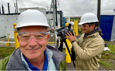 Two men with hard hats stand outside in front of equipment