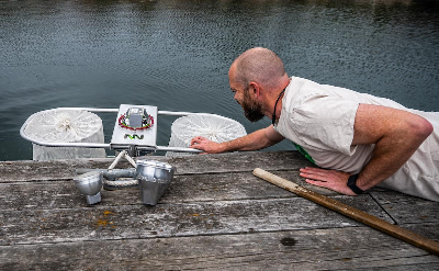 A man leans off of a dock to reach equipment in a lake