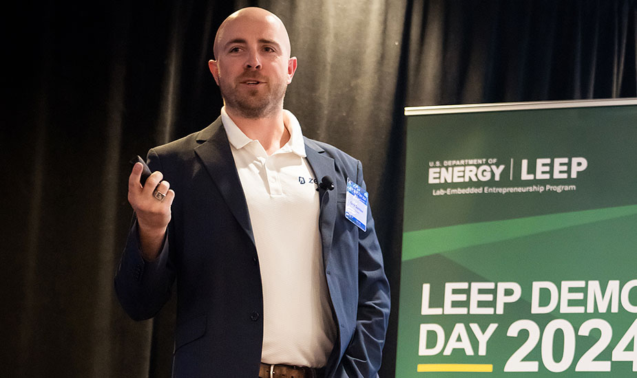 A person speaks and gestures while standing next to a sign bearing the words LEEP DEMO DAY 2024.