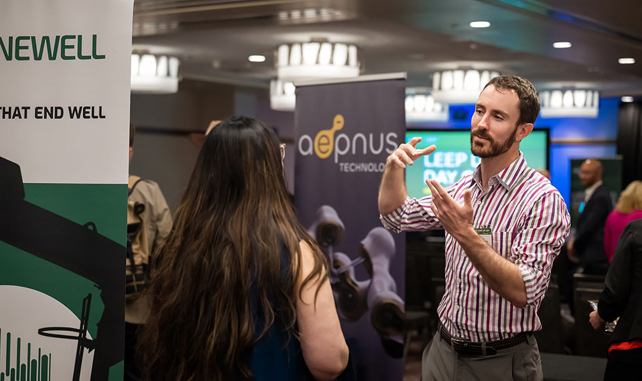 A person speaks and gestures with someone in a crowded expo room.