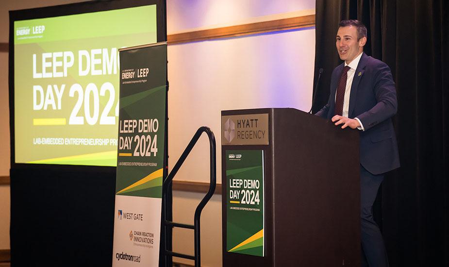 A person stands behind a podium next to a screen and signs bearing the words LEEP DEMO DAY 2024.