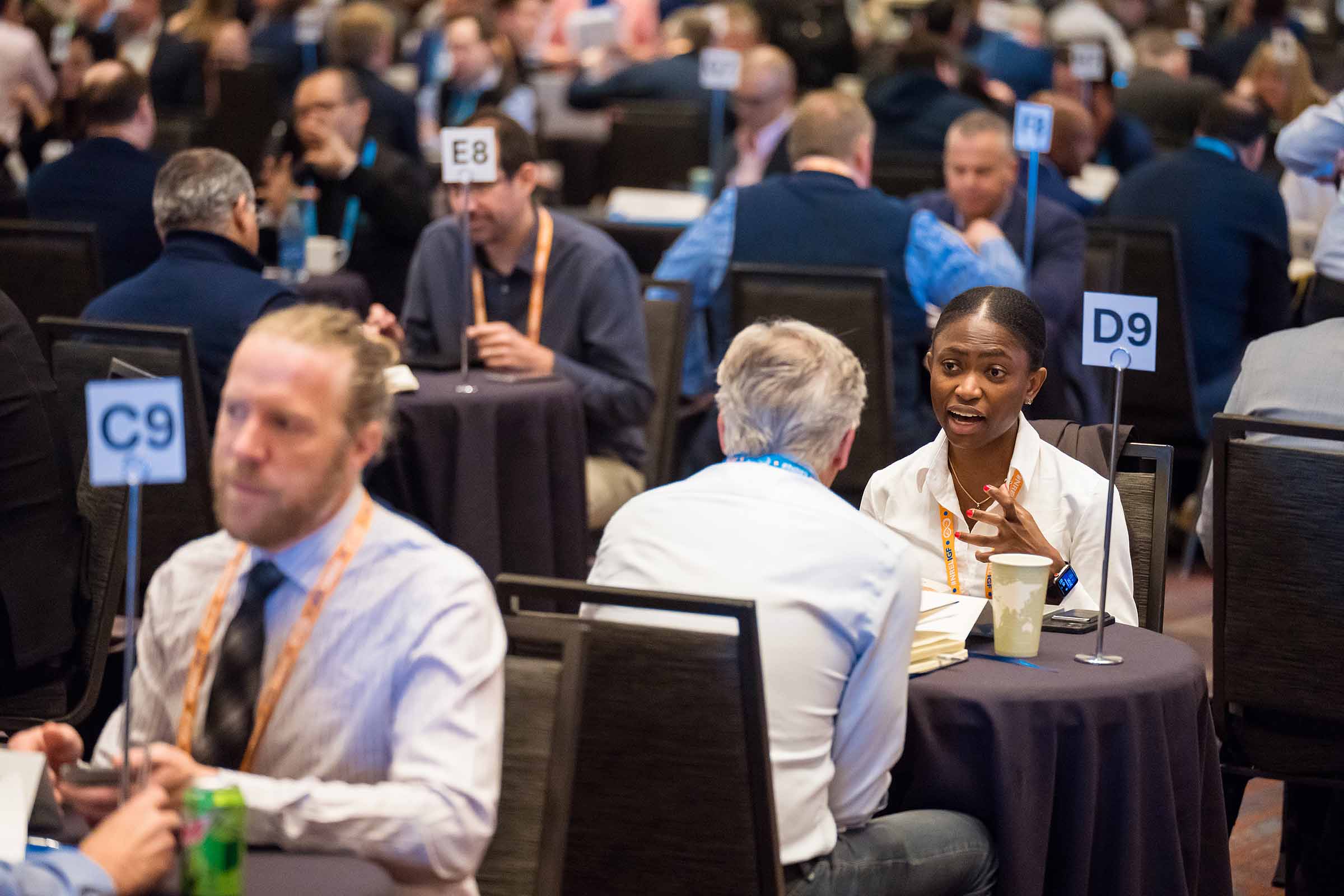 Two people sit at a small table for a meeting in a ballroom with dozens of similarly occupied small tables around them.