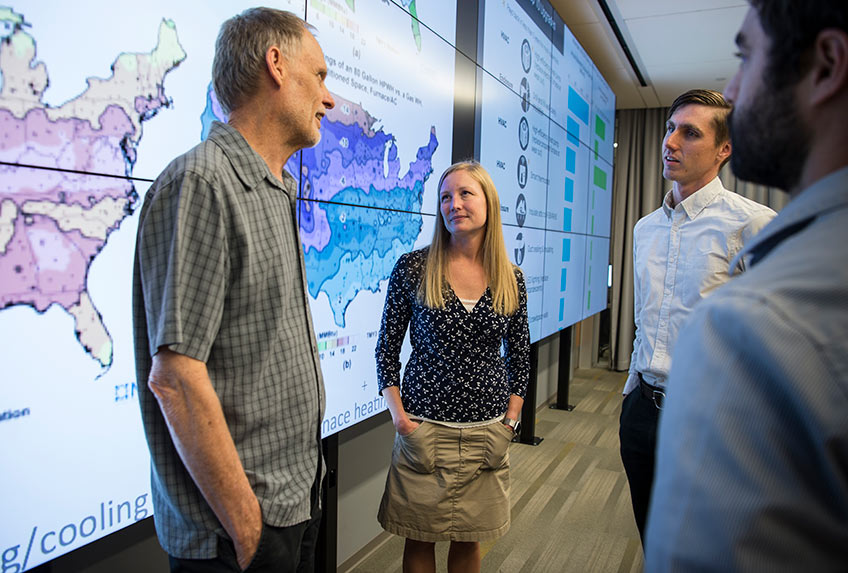 45443 A group of people stand in front of screens with maps and graphics displayed across them.