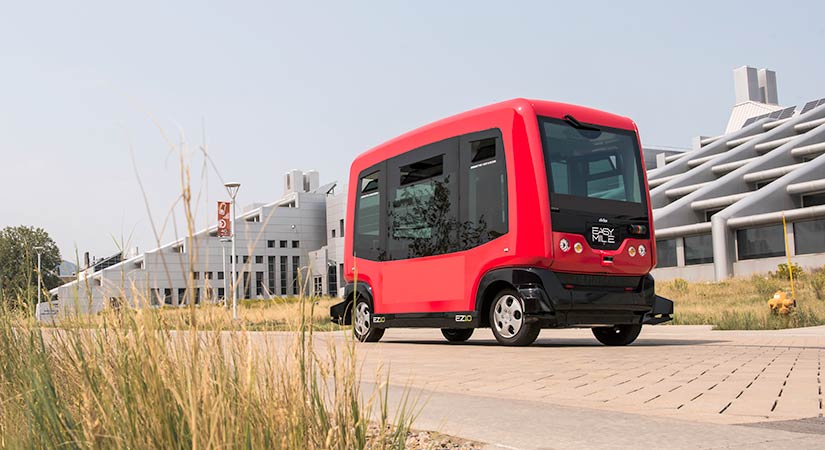 47296 A photo of a red all-electric shuttle bus driving on a road by a large building.