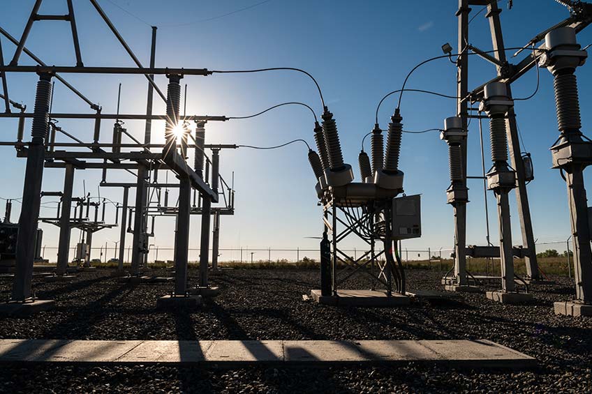 62259 The sun peaks through a power grid system, casting shadows on the ground.