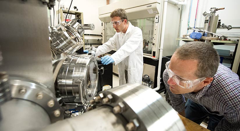 Two researchers wearing protective gear work in a lab setting.