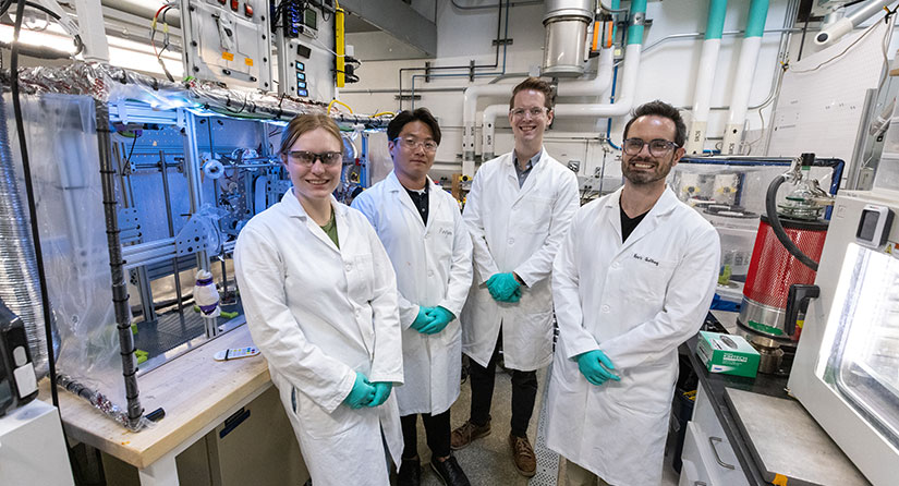 non-evaporative-drying-group Four people in lab coats stand in front of equipment in a lab.