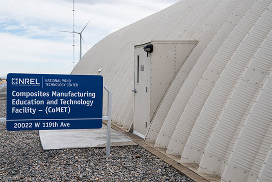 photo-comet-bldg-41790 Photo of a white dome-shaped building with a sign that says, 'Composites Manufacturing Education and Technology Facility – (CoMET ),' and a wind turbine in the background.