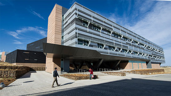 photo-esif-bldg-25300 Photo of a three-story, beige, grey, and black building with two people walking in front of it.