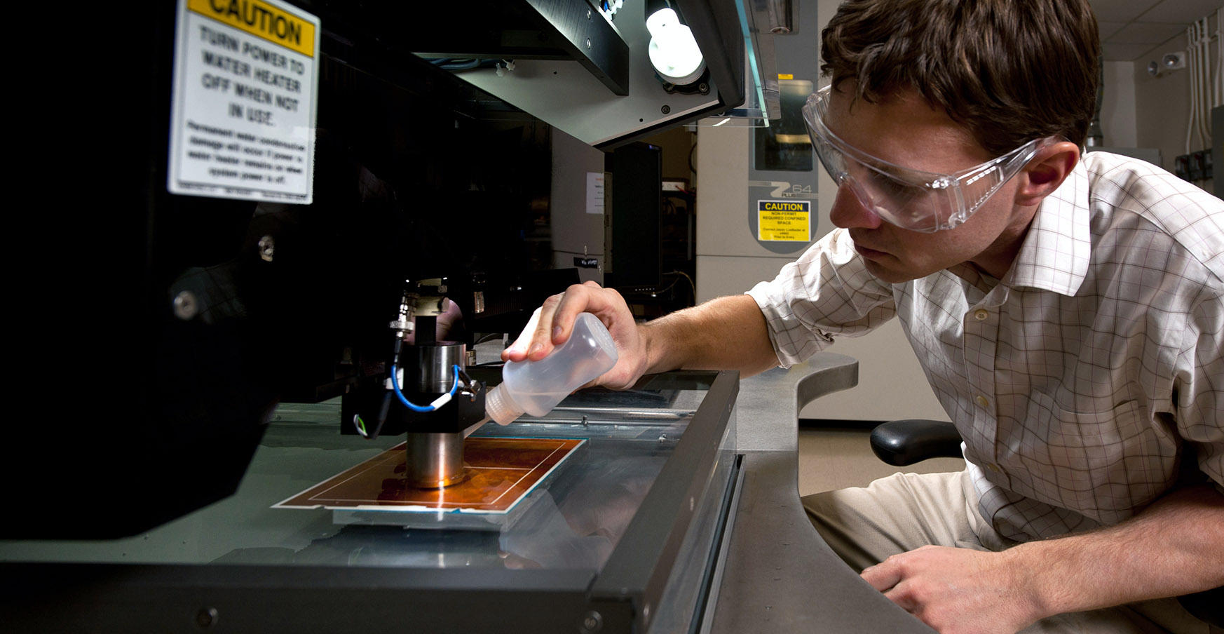 photo-hero-20036 Researcher applying a liquid on a plate below lab equipment.