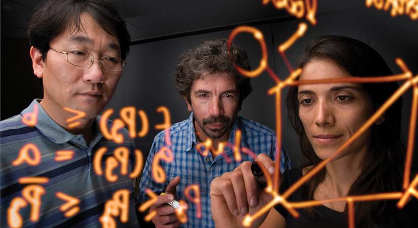 research-analysis-16560-lg A photo of a group of people writing equations in orange marker on a clear, plastic board.