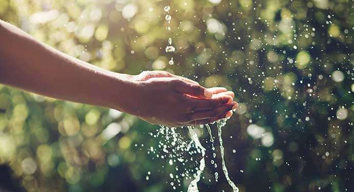 A photo of two hands catching water as it falls.