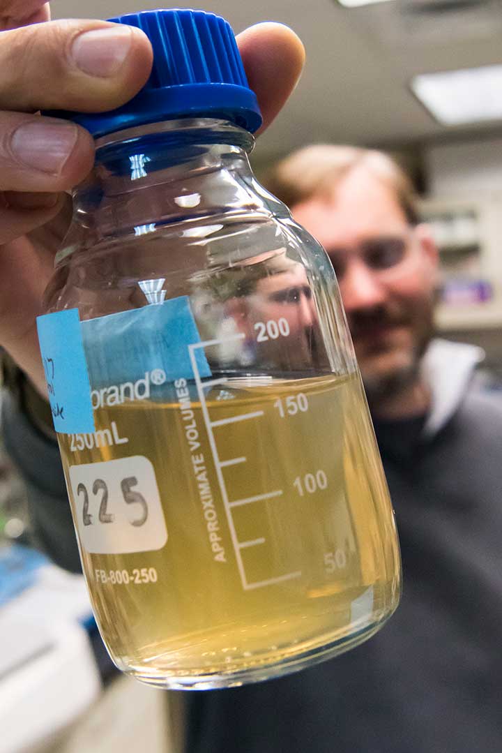 A scientist holds a glass container filled with a murky-looking liquid.