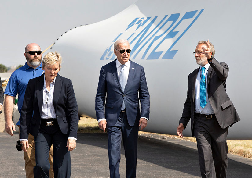 Four people walking and talking in front of a wind turbine blade