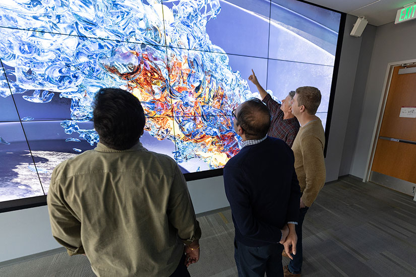 Four people pointing at a 3D screen.
