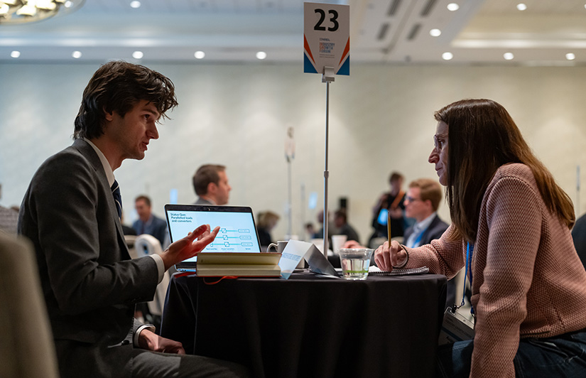 20250421-record-attendance-at-30th-annual-nrel-industry-growth-forum-as-innovation-soars-michael A man sits at a small table talking to a woman taking notes.
