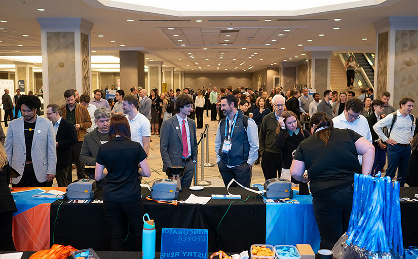 20250421-record-attendance-at-30th-annual-nrel-industry-growth-forum-as-innovation-soars-opening-reception Two men talk with hundreds of people behind them in a large hotel area.
