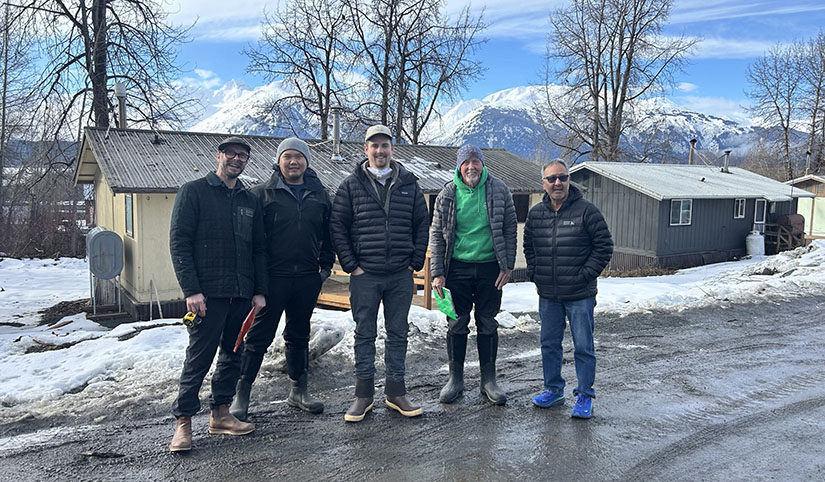 20250507-nrel-partners-with-chilkat-indian-village-to-improve-housing-in-alaska-group Five people stand on a road in front of a house.