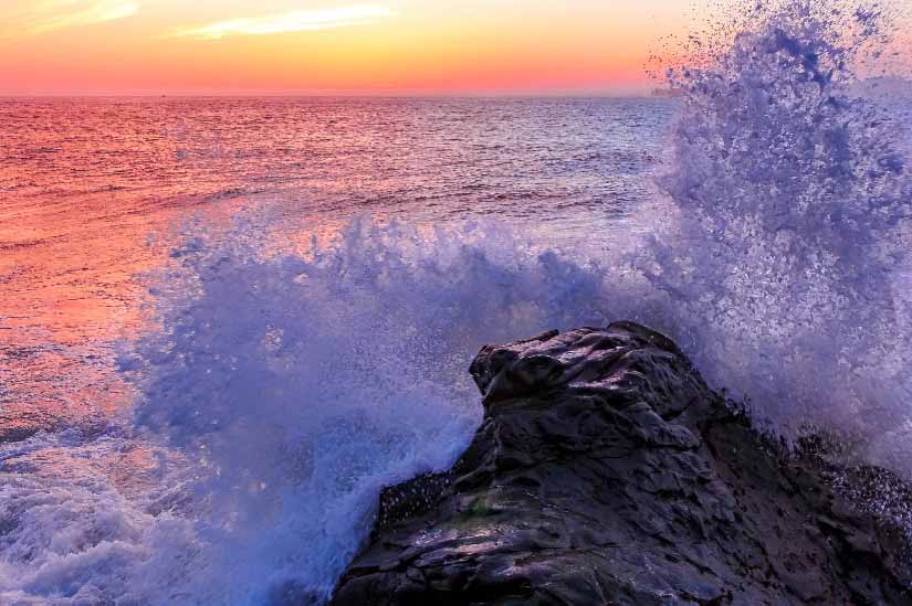 Wave crashing on rock at sunset