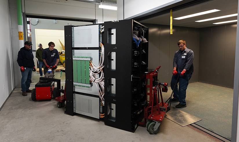 A group of people move a piece of the supercomputer via trolley cart into a room.