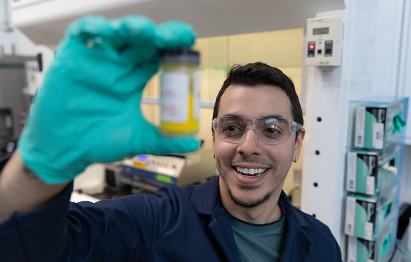 A person wearing gloves holds up a small glass container of liquid.
