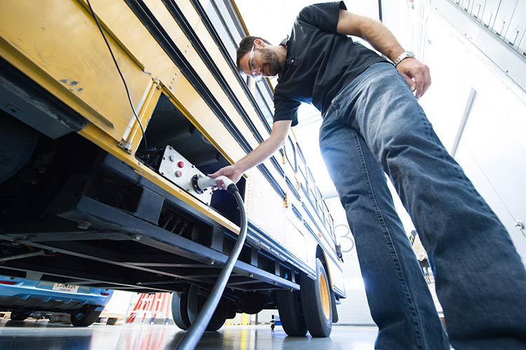 A man plugs a charging cable into an electric school bus.