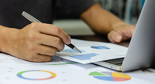 Close up a person working with a computer and printed charts.