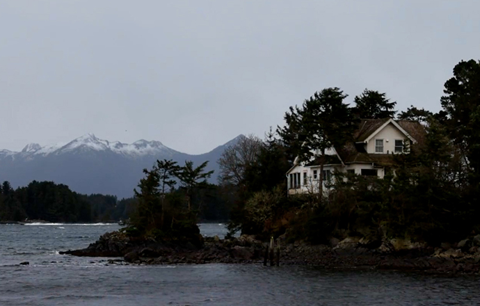 A house on a rocky coastline with mountains in the background.