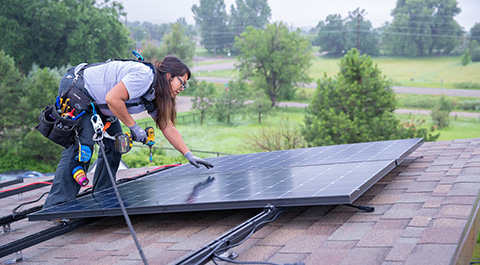 A woman installing a solar panel on a roof.