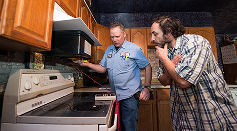 Two men in a kitchen examining a stove top.