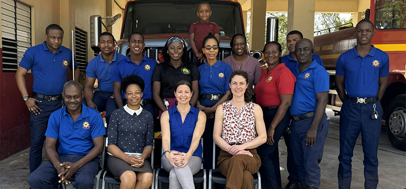 Group of individuals stand and sit in front of firetruck.