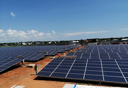 Person walks alongside solar panels on the ground.