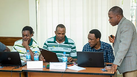 Four people look at laptop computers inside conference room.