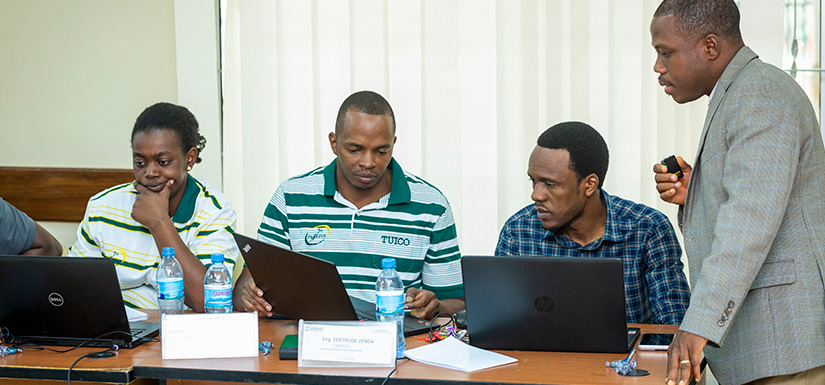 Four people work together over computers on desk.