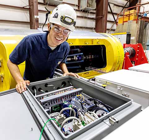 An engineer in a hard hat leaning over an open hatch full of wires