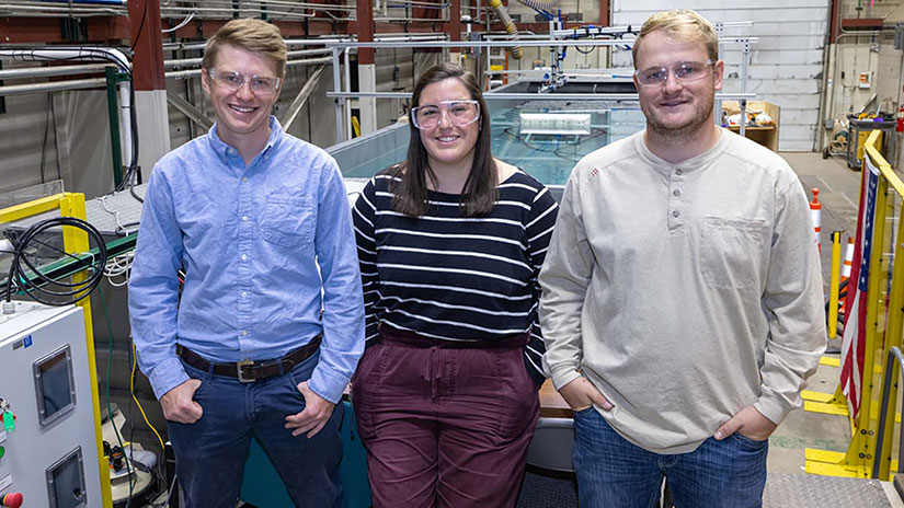Three people stand inside lab in front of wave pool